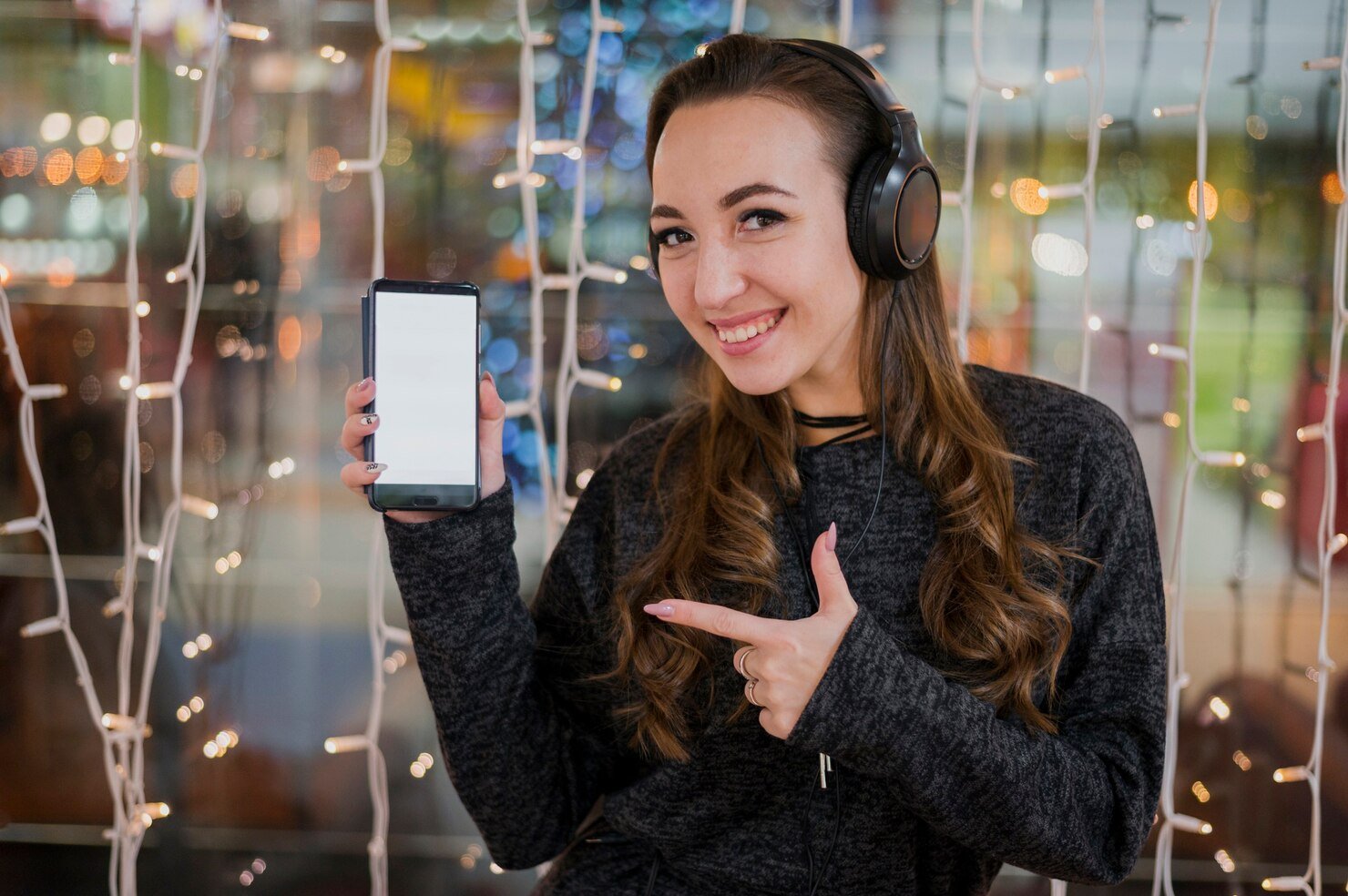 woman-wearing-headphones-showing-phone-near-christmas-lights_23-2148397201